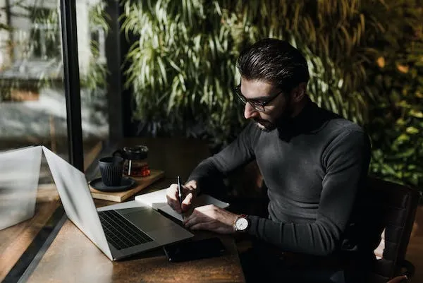 Business owner writing an invoice in a notebook next to a laptop